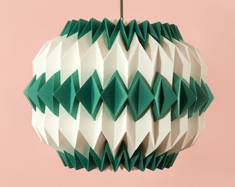 Könnte beinhalten: Eine weiße und grüne Hängelampe im Origami-Stil hängt an der Decke vor einer hellrosa Wand. Eine klare Glasvase mit strukturierter Oberfläche hält zwei grüne Blätter.