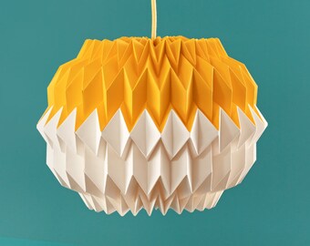 Könnte beinhalten: Ein gelber und weißer Lampenschirm im Origami-Stil hängt an einem Kabel vor einem türkisfarbenen Hintergrund. Der Lampenschirm ist aus Papier gefertigt und hat ein geometrisches Design.