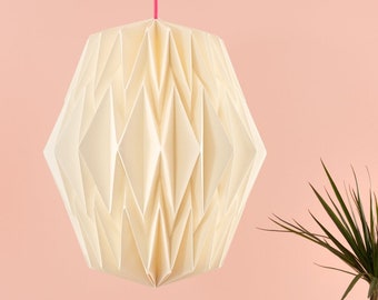 Könnte beinhalten: Eine weiße Pendelleuchte im Origami-Stil hängt an einem rosa Kabel vor einer hellrosa Wand. Eine Topfpflanze mit grünen Blättern steht auf einer hellrosa Oberfläche.