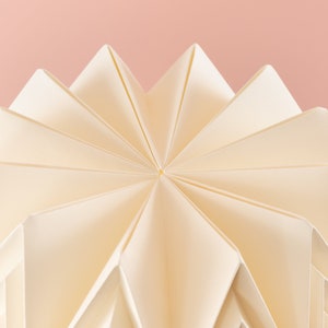 Puede incluir: Una pantalla de l&aacute;mpara de origami blanca con un patr&oacute;n de estrella. La pantalla est&aacute; doblada en una serie de puntos que crean un dise&ntilde;o geom&eacute;trico.