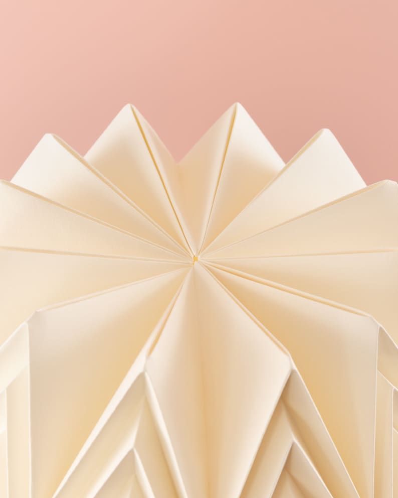 Puede incluir: Una pantalla de l&aacute;mpara de origami blanca con un patr&oacute;n de estrella. La pantalla est&aacute; doblada en una serie de puntos que crean un dise&ntilde;o geom&eacute;trico.