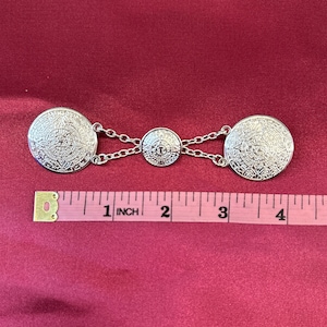 May include: Silver tone metal clasp with two round Aztec calendar designs and a smaller round center piece. The clasp measures approximately 4 inches long.