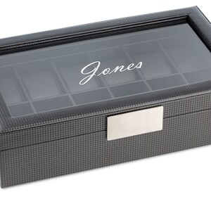 May include: A black leather watch box with a glass top and a silver nameplate. The box has a grid pattern and the name "Jones" is engraved on the top.