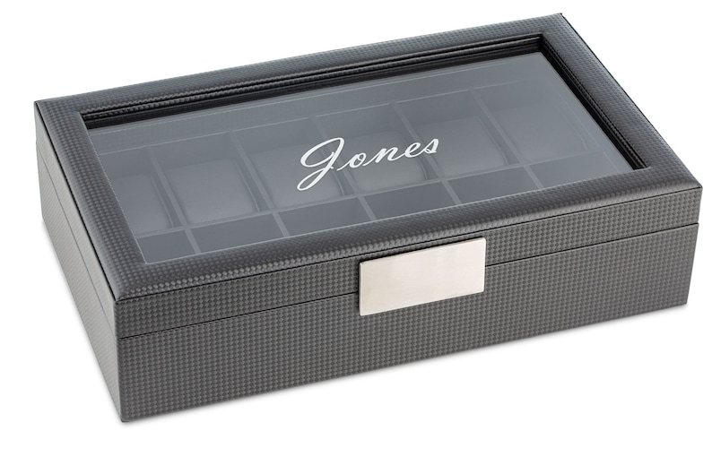 May include: A black leather watch box with a glass top and a silver nameplate. The box has a grid pattern and the name "Jones" is engraved on the top.