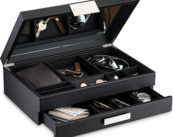 May include: A black, multi-compartment valet box with a carbon fiber pattern. The open box reveals a mirrored lid, sunglasses, a wallet, keys, coins, a watch, and a drawer with cash. The box has a silver-colored handle.