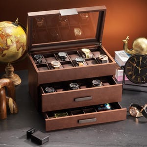 May include: A brown leather watch box with a glass top, holding various wristwatches. The box has two drawers and is displayed with a globe, a clock, and other decorative items. The watches are of different styles and colors.