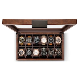 May include: A brown wooden watch box with a glass top. The box has 12 compartments, each with a black cushion to hold a watch. The box is open and there are 12 watches inside.