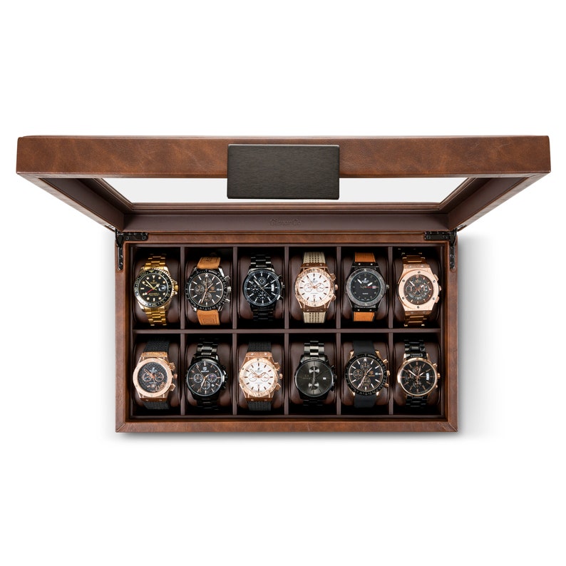 May include: A brown wooden watch box with a glass top. The box has 12 compartments, each with a black cushion to hold a watch. The box is open and there are 12 watches inside.