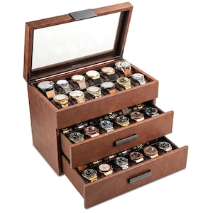 May include: A brown faux leather watch box with a glass lid and two pull-out drawers. The interior features multiple compartments, each holding a wristwatch with various metal bands and faces. The box has black metal handles and hinges.