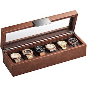 May include: A brown leather watch box with a clear glass top, displaying six assorted wristwatches. The watches feature gold, silver, and black tones with various band styles. The box has a rectangular shape with a hinged lid and a silver metal clasp.