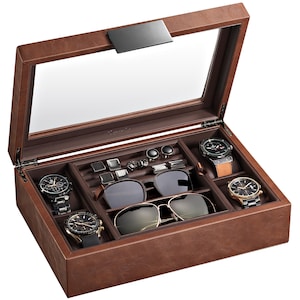 May include: A brown leather watch and accessory box with a glass top. The box contains several watches, sunglasses, cufflinks, and other accessories. The watches have black and gold faces and leather or metal bands. The sunglasses have dark lenses.