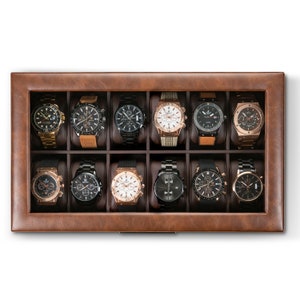 May include: A brown leather watch box with twelve compartments, each containing a different wristwatch. The watches have various styles, colors, and materials, including gold, silver, and black.