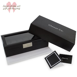 May include: Black leather watch box with a glass top and a silver nameplate that reads "Glenor Co.". The box is open and the lid is laying on top of the box. There is a small black card with the same logo on it.
