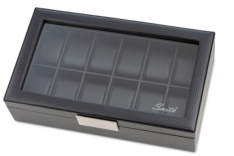 May include: A black watch box with a glass top and 12 compartments. The box has a carbon fibre pattern and the word "Smith" is engraved on the front.