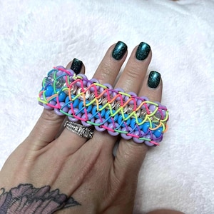 May include: A colorful beaded bracelet with a woven design. The bracelet features blue, purple, pink, yellow, and clear beads. The bracelet is approximately 1.5 inches wide.