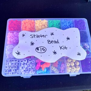 Könnte beinhalten: Ein klarer Kunststoff-Organizer gefüllt mit bunten Perlen. Die Perlen haben verschiedene Formen und Farben, darunter Rot, Orange, Gelb, Grün, Blau und Lila. Ein Papierschild liest "Starter Bead Kit."