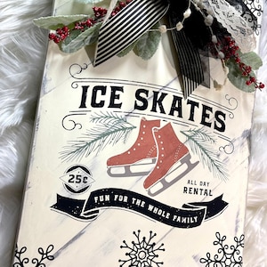 May include: A white wooden sign with black and white lettering that reads "Ice Skates, 25c, All Day Rental, Fun for the Whole Family". The sign features a pair of red ice skates, a pine branch, and snowflakes.