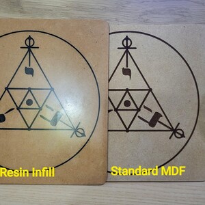 May include: Two square, light brown wooden panels with a geometric design in dark brown. One panel is labeled "Resin Infill" and the other "Standard MDF". The design features a triangle within a circle, with additional shapes and symbols.