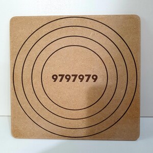 May include: Square wooden target board with concentric circles and the number "9797979" etched in the center. The board is a light brown color.