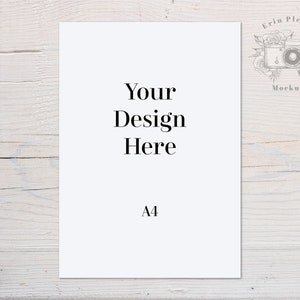 以下が含まれることがあります： 白い紙に「Your Design Here」と「A4」の文字が印刷されています。紙は白い木製の表面に置かれています。