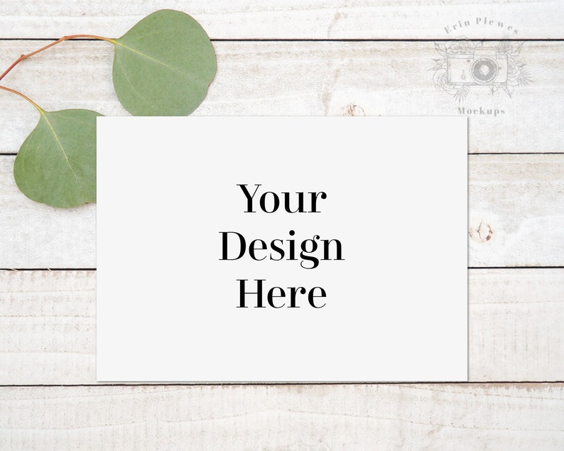 Puede incluir: Una tarjeta blanca con el texto "Your Design Here" sobre un fondo de madera blanqueada con hojas de eucalipto.