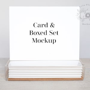 Puede incluir: Una maqueta de tarjeta blanca con el texto "Card & Boxed Set Mockup" que se muestra en la parte superior de una pila de tarjetas blancas en una caja de acrílico transparente.