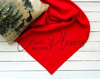 May include: A red blanket with a folded edge is draped over a white wooden surface. A pillow with a brown and green deer print is partially visible in the upper left corner. The text "Erin Plewes Mockups" is written in black cursive on the blanket.