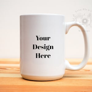 May include: A large white ceramic mug with a curved handle. The mug has the text "Your Design Here" in a bold, black font. The mug is sitting on a light-colored wooden surface.