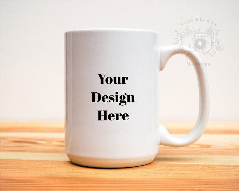May include: A large white ceramic mug with a curved handle. The mug has the text "Your Design Here" in a bold, black font. The mug is sitting on a light-colored wooden surface.