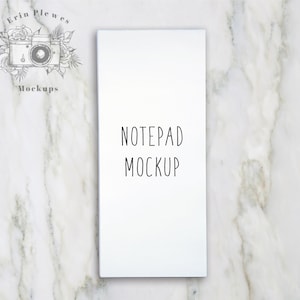 Op de afbeelding: Witte notitieblok mockup op een marmeren achtergrond. Het notitieblok heeft de tekst "NOTEPAD MOCKUP" erop staan.