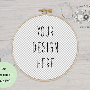 Pode incluir: Um aro de bordado de madeira com fundo branco e o texto "YOUR DESIGN HERE" em preto. O aro está sobre uma superfície de madeira branca.