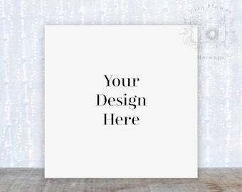 May include: White square card mockup with the text "Your Design Here" on a white background with a blurry white and silver background.