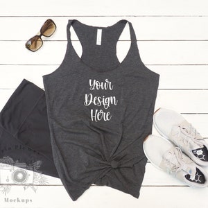 May include: A dark gray racerback tank top with the text "Your Design Here" printed on the front. The tank top is laying flat on a white wooden surface.