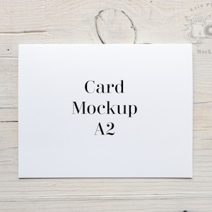 Puede incluir: Una maqueta de tarjeta blanca sobre un fondo de madera clara. La tarjeta está en blanco y tiene el texto "Card Mockup A2" impreso en ella.