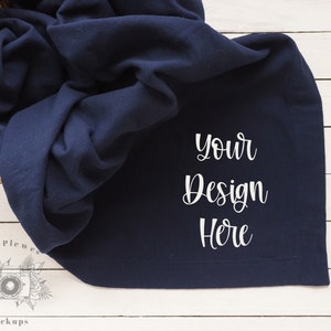 May include: A navy blue blanket with the text "Your Design Here" in white on a white wood background.