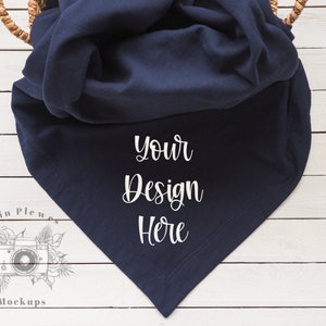 May include: A navy blue blanket with the text "Your Design Here" is draped over a woven basket. The blanket is folded in a triangular shape, with a white wooden surface in the background.