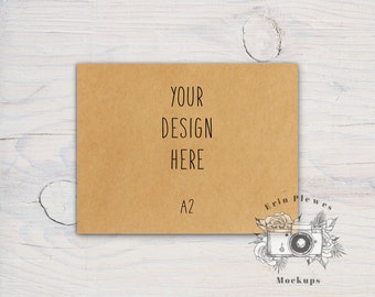 Puede incluir: Una maqueta de papel marrón con el texto "YOUR DESIGN HERE" y "A2" impreso en ella. El papel está sobre un fondo de madera blanca.