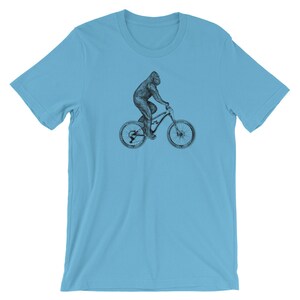 Puede incluir: Una camiseta azul claro con una ilustraci&oacute;n en blanco y negro de un gorila montando una bicicleta de monta&ntilde;a.