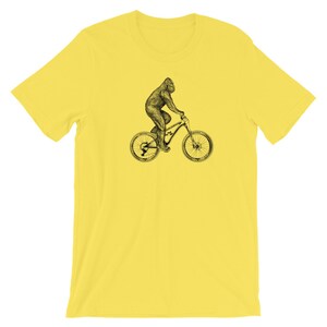 Puede incluir: Una camiseta amarilla con una ilustraci&oacute;n en blanco y negro de un gorila montando una bicicleta de monta&ntilde;a.
