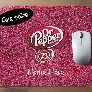 Puede incluir: Alfombrilla de ratón rectangular con superficie rosa brillante. El logotipo de Dr Pepper está centrado, con el texto "Name Here" debajo. Un ratón de ordenador blanco descansa en el lado derecho, y la palabra "Personalize" está en un óvalo negro.