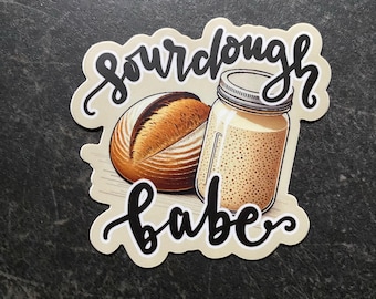 May include: A sticker with a sourdough bread loaf and a jar of sourdough starter. The sticker has the text "sourdough babe" in black cursive.