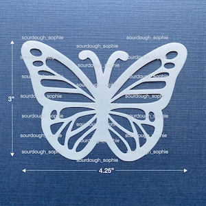 May include: A white butterfly-shaped craft with intricate cut-out details. The butterfly measures 4.25 inches wide and 3 inches tall. The text "sourdough_sophie" is repeated across the image.