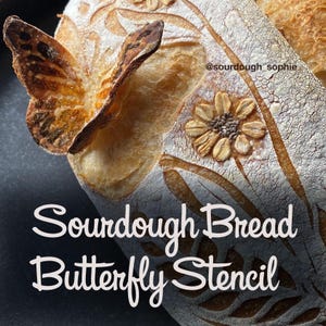 May include: A loaf of sourdough bread with a butterfly stencil and a flower design. The bread is golden brown with a textured crust. The text "Sourdough Bread Butterfly Stencil" is visible.