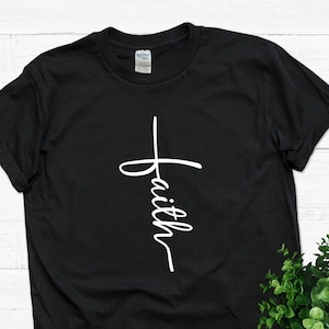 Puede incluir: Camiseta negra con una cruz blanca y la palabra "faith" escrita verticalmente.
