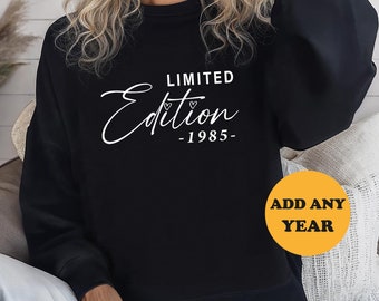 May include: Black sweatshirt with white text that reads "LIMITED Edition -1985-" and a small heart symbol. The text "ADD ANY YEAR" is on a yellow circle.