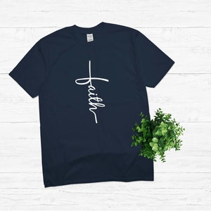 Puede incluir: Una camiseta azul marino con una cruz blanca y la palabra "faith" escrita verticalmente en ella.