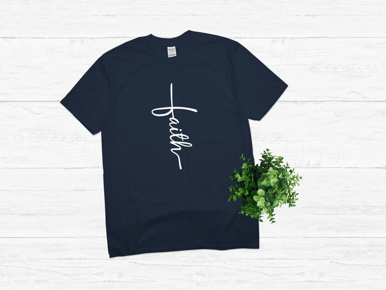 Puede incluir: Una camiseta azul marino con una cruz blanca y la palabra "faith" escrita verticalmente en ella.