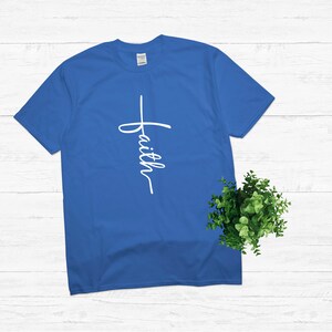 Puede incluir: Una camiseta azul real con una cruz blanca y la palabra "faith" escrita verticalmente en ella.