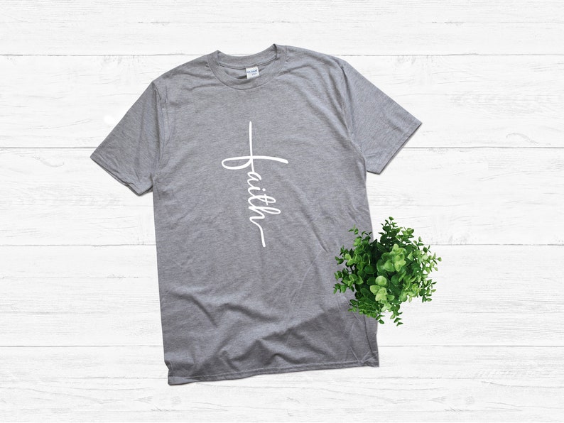 Puede incluir: Una camiseta gris jaspeada con una cruz blanca y la palabra "faith" escrita verticalmente en ella.