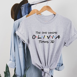 May include: Gray t-shirt with the text "The One Where Olivia Turns 30" in black with colorful dots. The text is styled like the title cards from the TV show Friends.